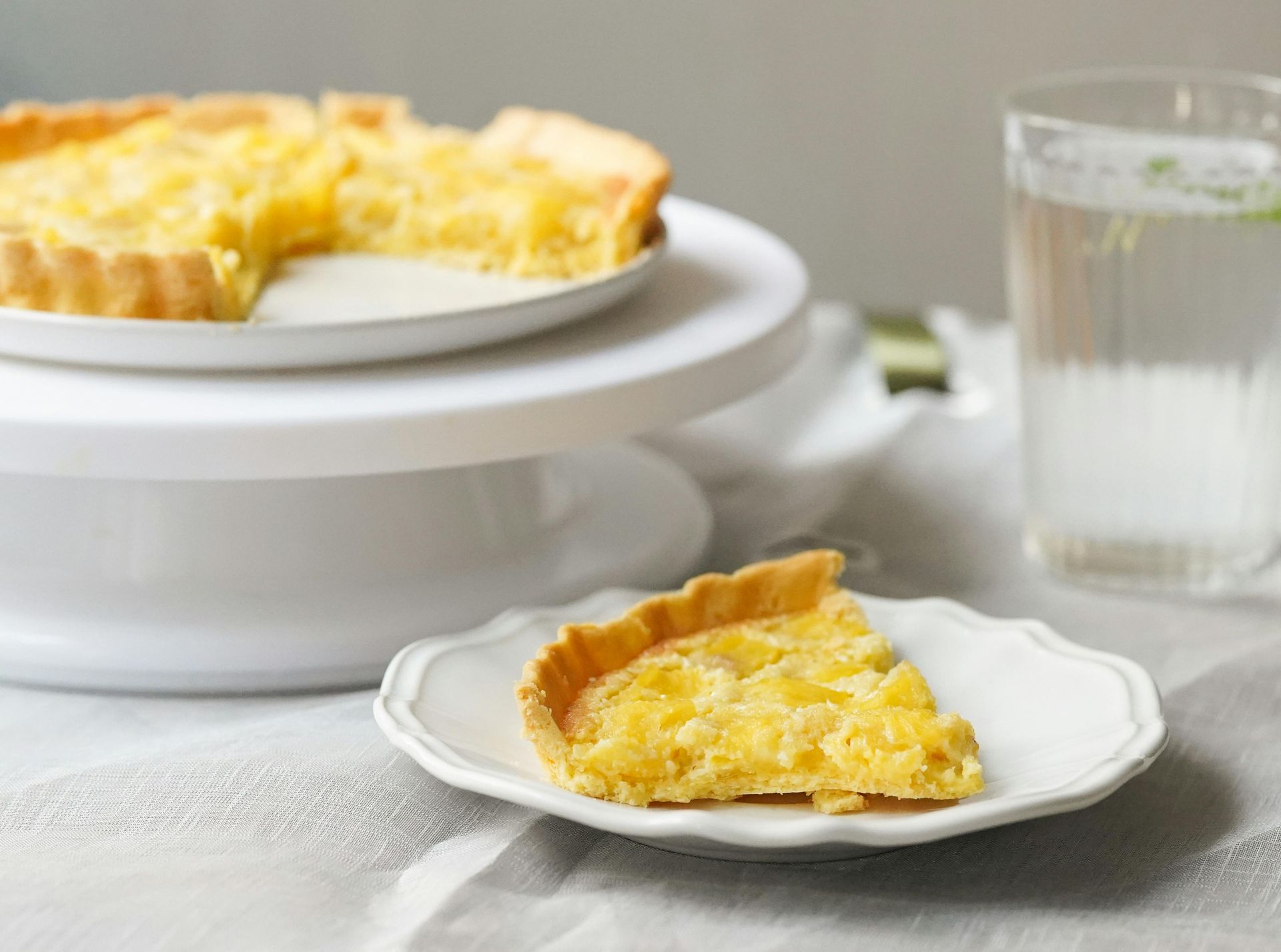 A slice of pie is on a white plate next to a glass of water.