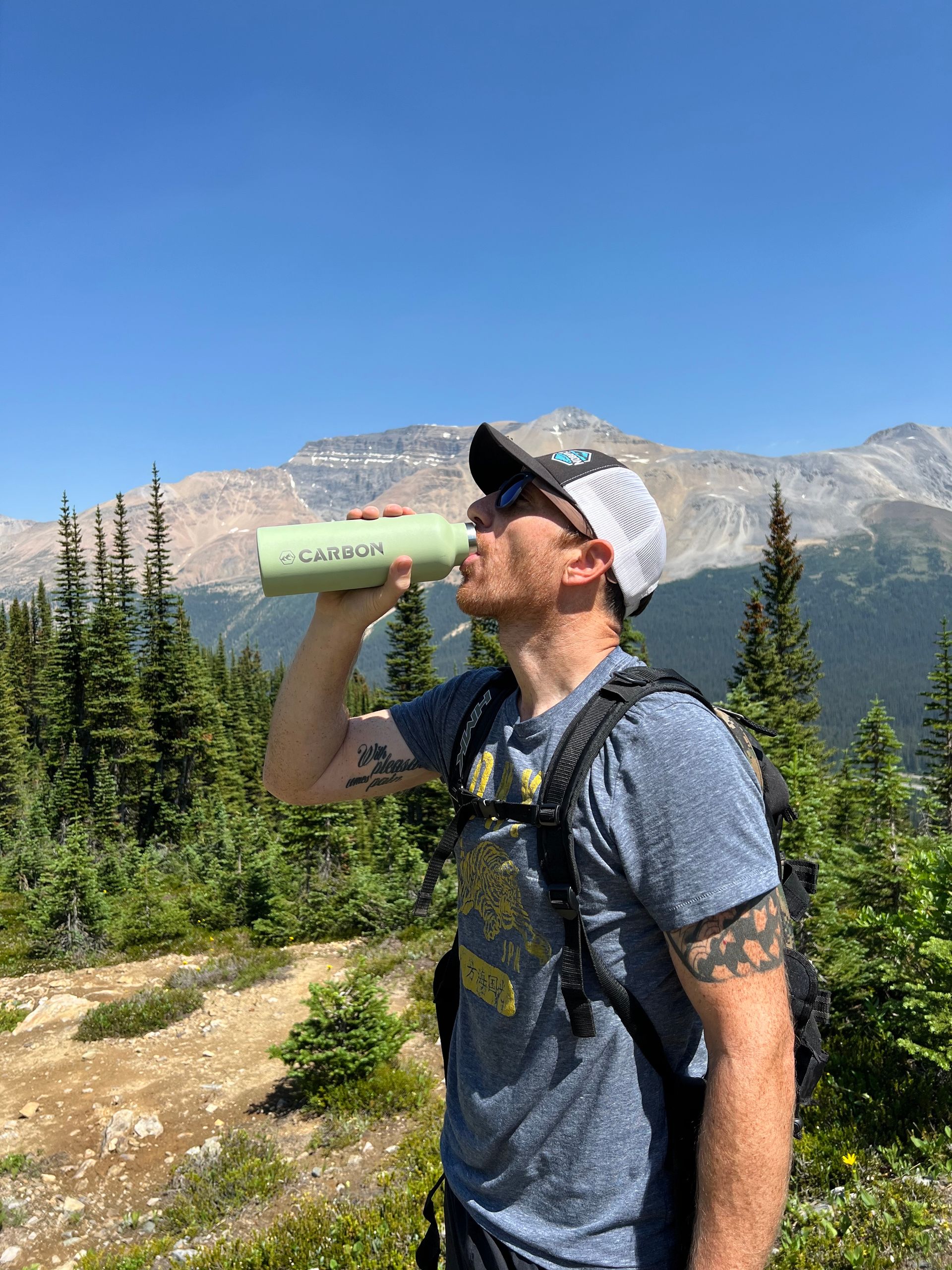 A man is drinking water from a bottle on top of a mountain.
