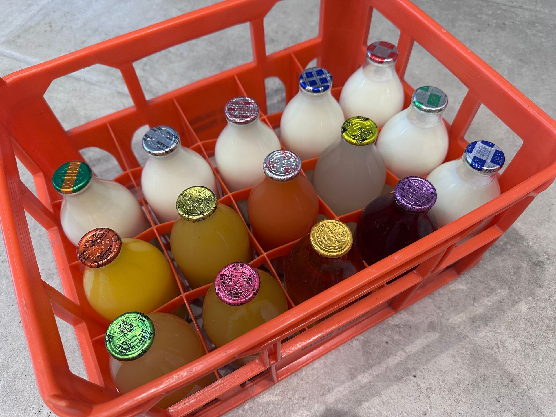 A plastic crate filled with assorted juice and milk bottles featuring colorful, patterned caps.