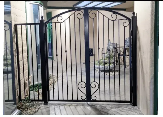 Black wrought-iron gate and side gate in front of a courtyard with a fountain and seating.