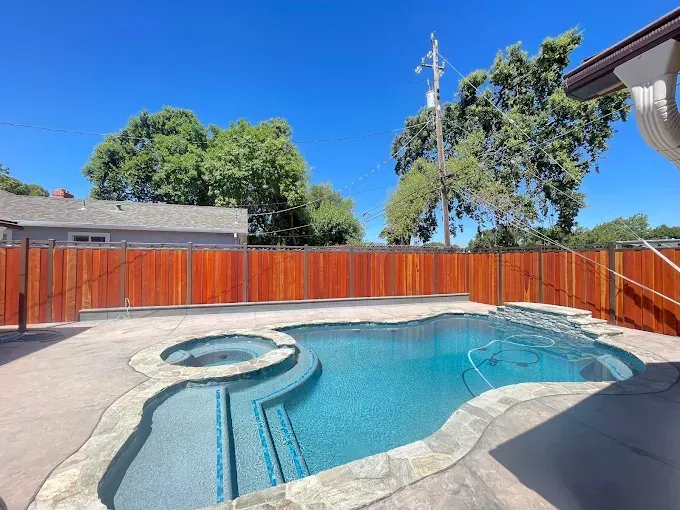 Pool and spa surrounded by concrete patio and redwood fence on a sunny day.