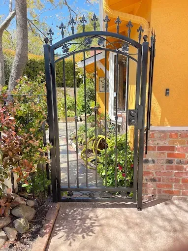 Black wrought-iron gate in a brick and stucco building entrance, plants surround.