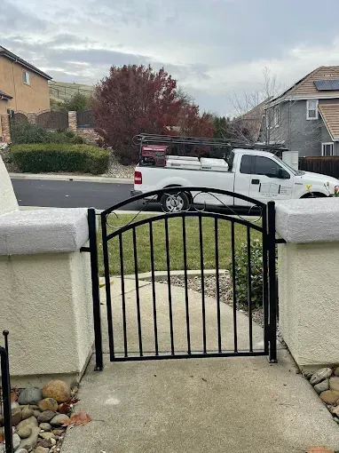 Black metal gate in a concrete walkway, with a white truck in the background, cloudy sky.