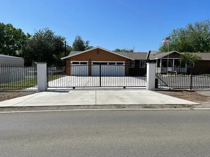 A brown house with a closed black gate and white pillars, set against a blue sky.