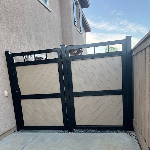 Black and tan double gate with diagonal wood paneling, set between a stucco wall and wooden fence.