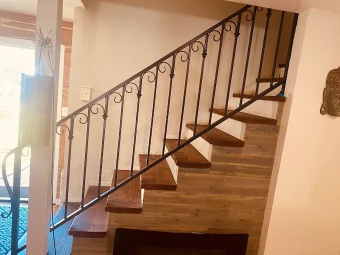 Staircase with wooden steps and black wrought iron railing against a light-colored wall.