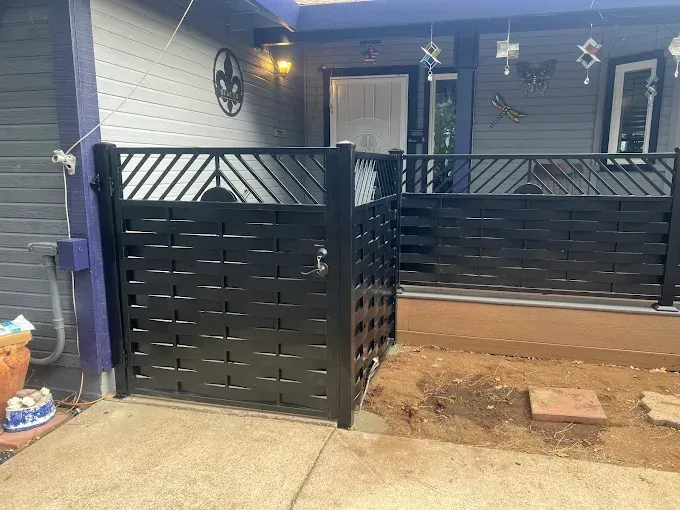 Black privacy fence with decorative diagonal and woven sections; concrete patio.