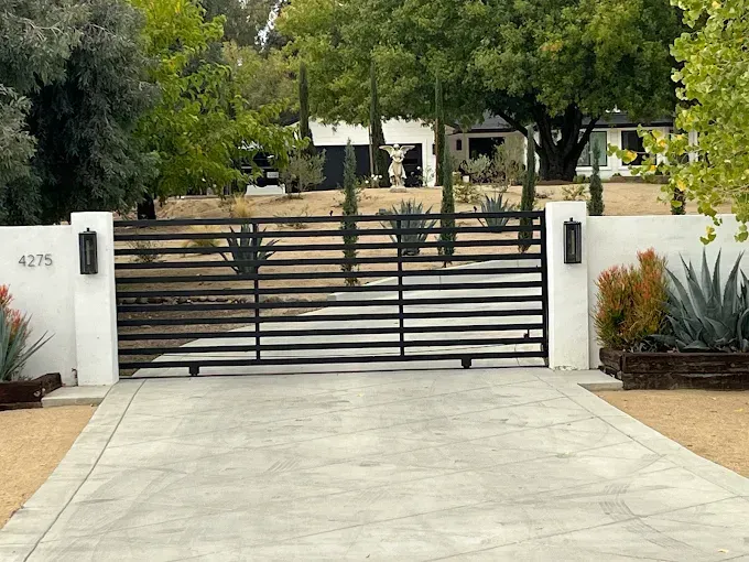 Driveway with a black gate, white walls, and a modern house in the background.