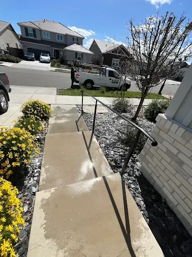 Concrete steps with a handrail leading up to a house. A white truck parked in the street.