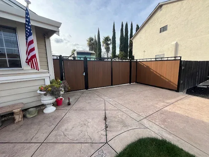 Fenced patio with brown panels, black posts, American flag, and beige house on a cloudy day.