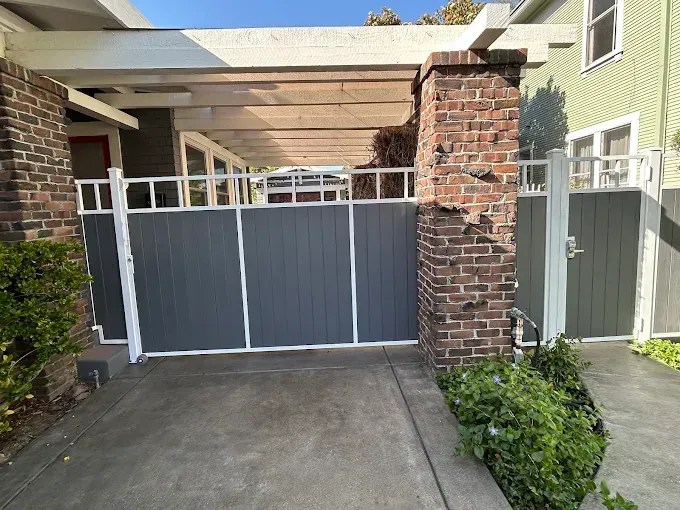 Gray gate with white trim in front of a house. Brick columns and a pergola are visible.
