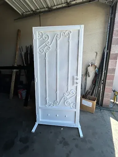 White metal door with decorative scrollwork, standing in a workshop.