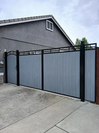 Gray wooden fence with black metal frame and gate in front of a house.