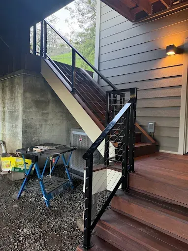Outdoor wooden staircase with black railing and cable infill, ascending to a deck under an eave.