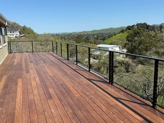 Wooden deck with black railing overlooking a valley on a sunny day.