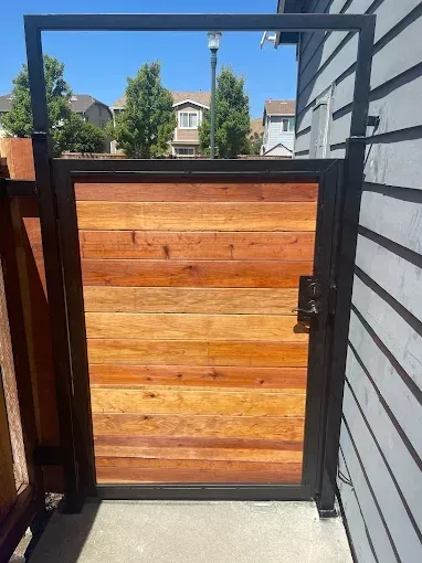 Black metal gate with horizontal wooden planks, beside a gray building.