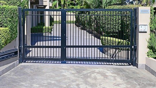 Black metal driveway gate, vertical bars, opening to a driveway.