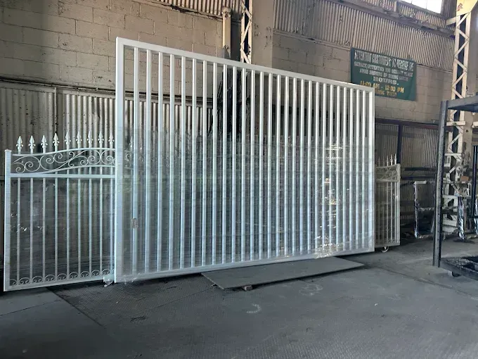 Metal gates in a workshop setting, vertical bars and decorative elements, painted silver.