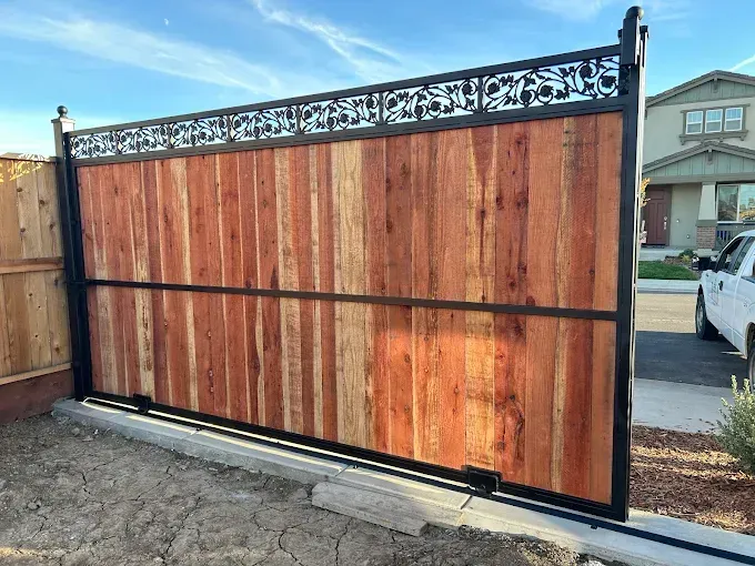 Wooden gate with decorative black metalwork in front of a house, on a sunny day.