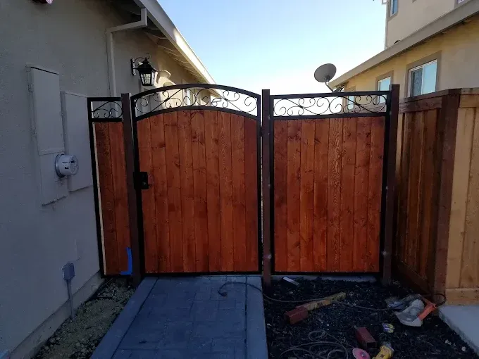 Wooden double gate with arched top, framed in black metal, in a backyard setting.