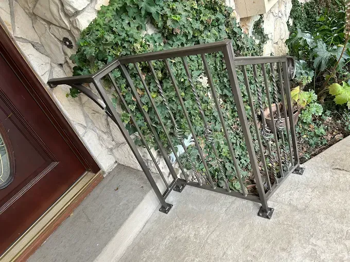 Metal handrail next to a door, on a concrete porch, with surrounding greenery.