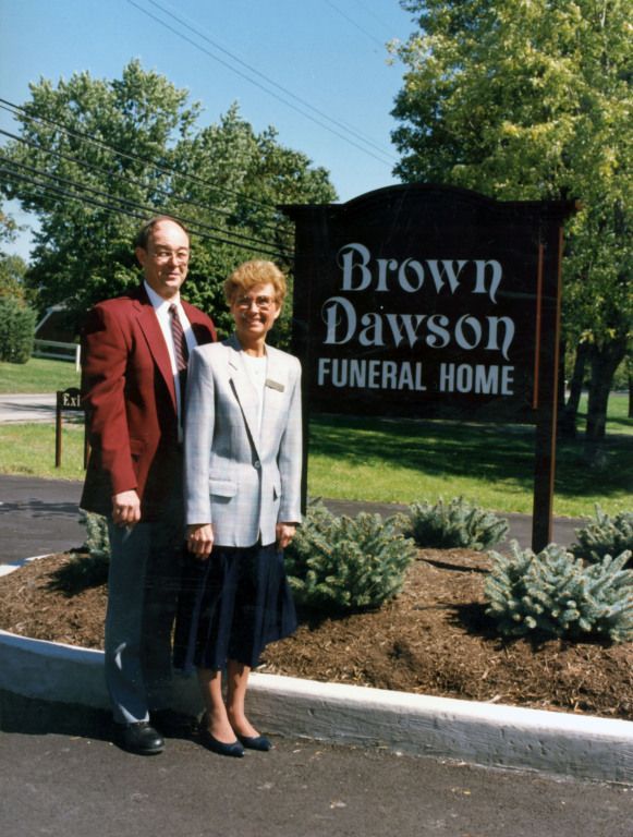 A man and woman stand in front of a brown dawson funeral home sign