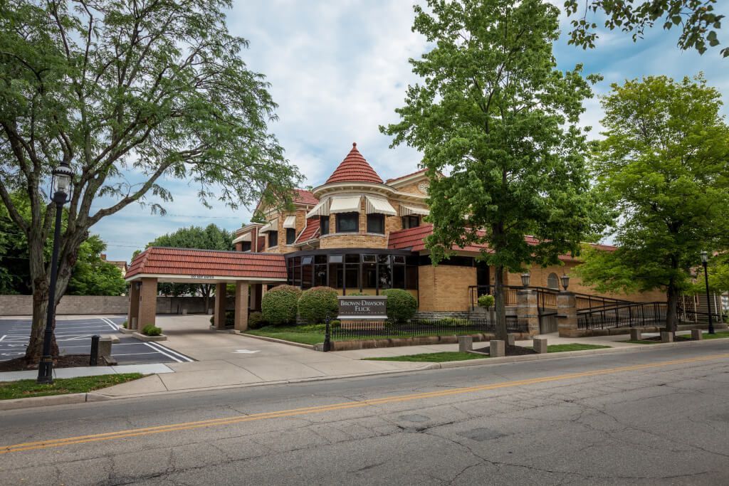 A large building with a red roof is surrounded by trees and a parking lot.