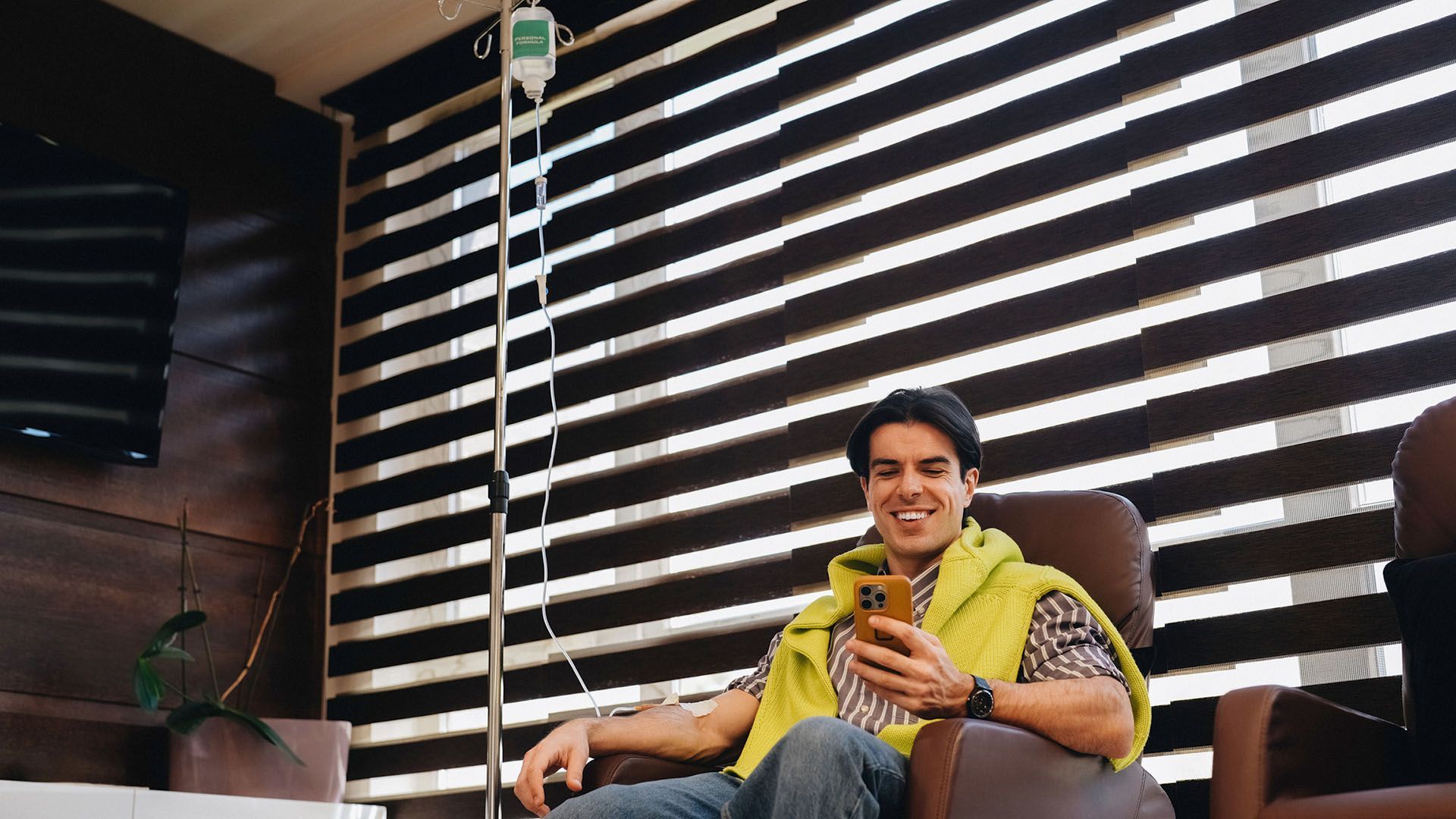 Man receiving an IV drip while smiling at his phone
