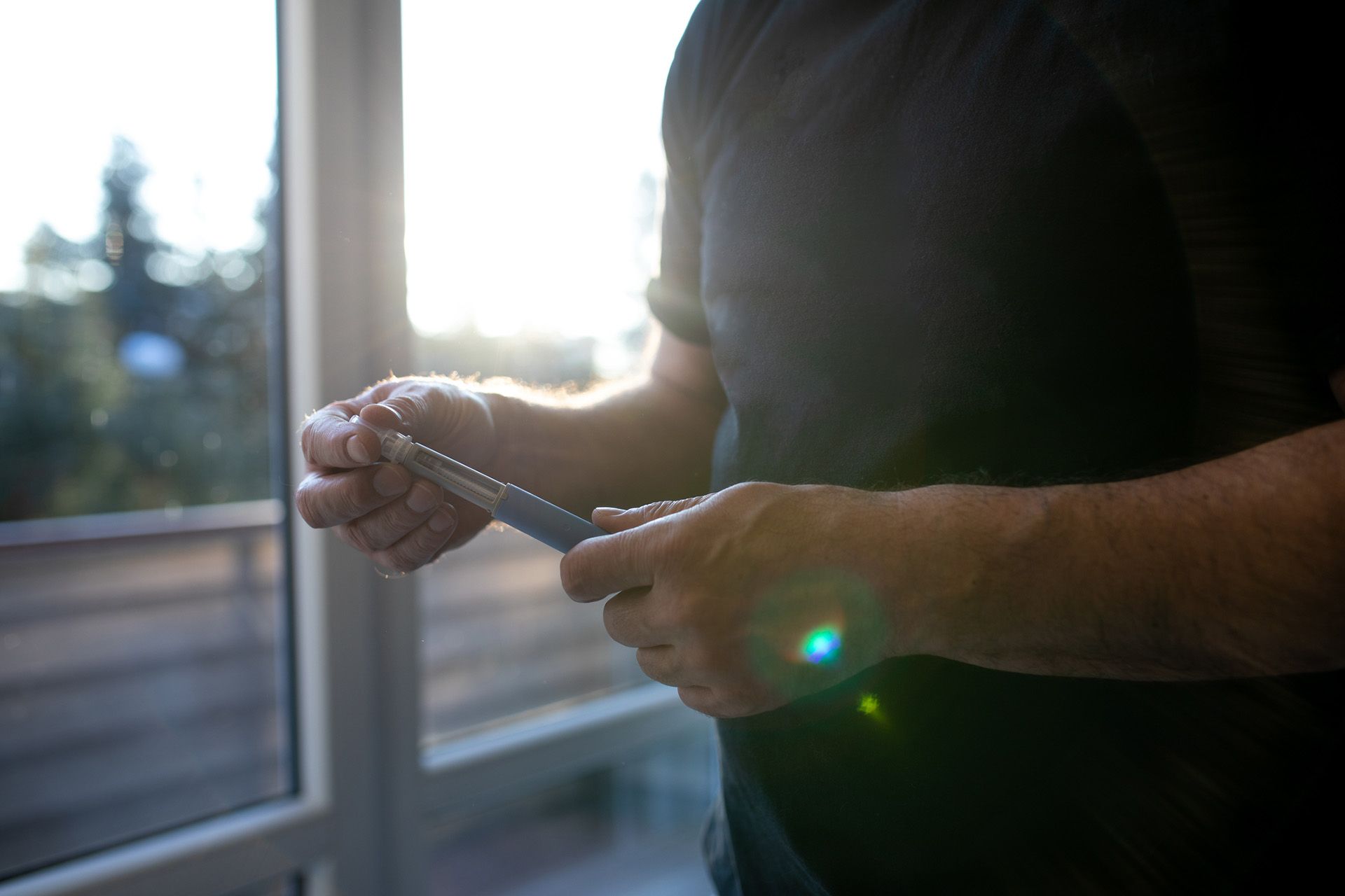 Person holding a blue insulin pen near a window