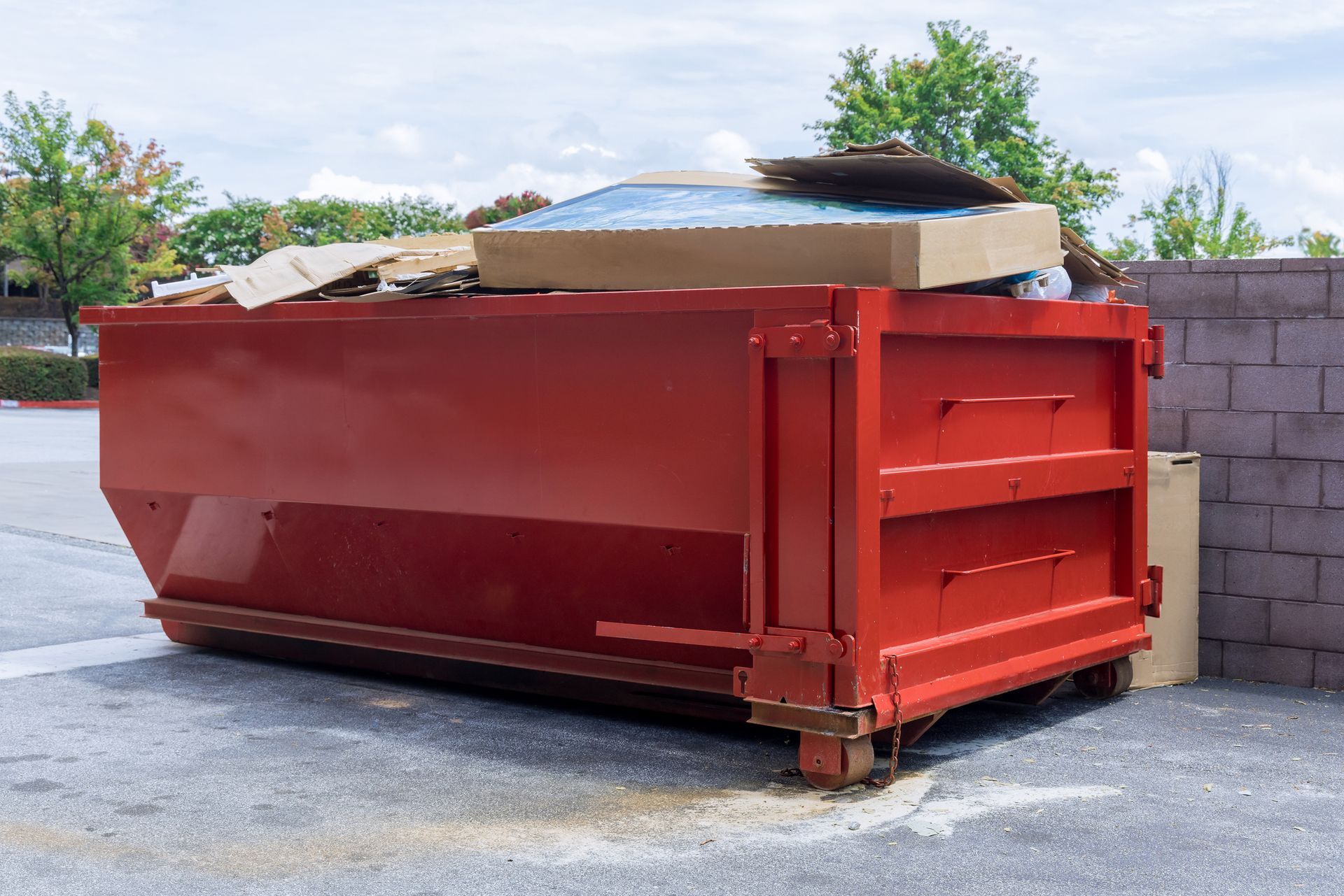 A red dumpster filled with cardboard is sitting in a parking lot.