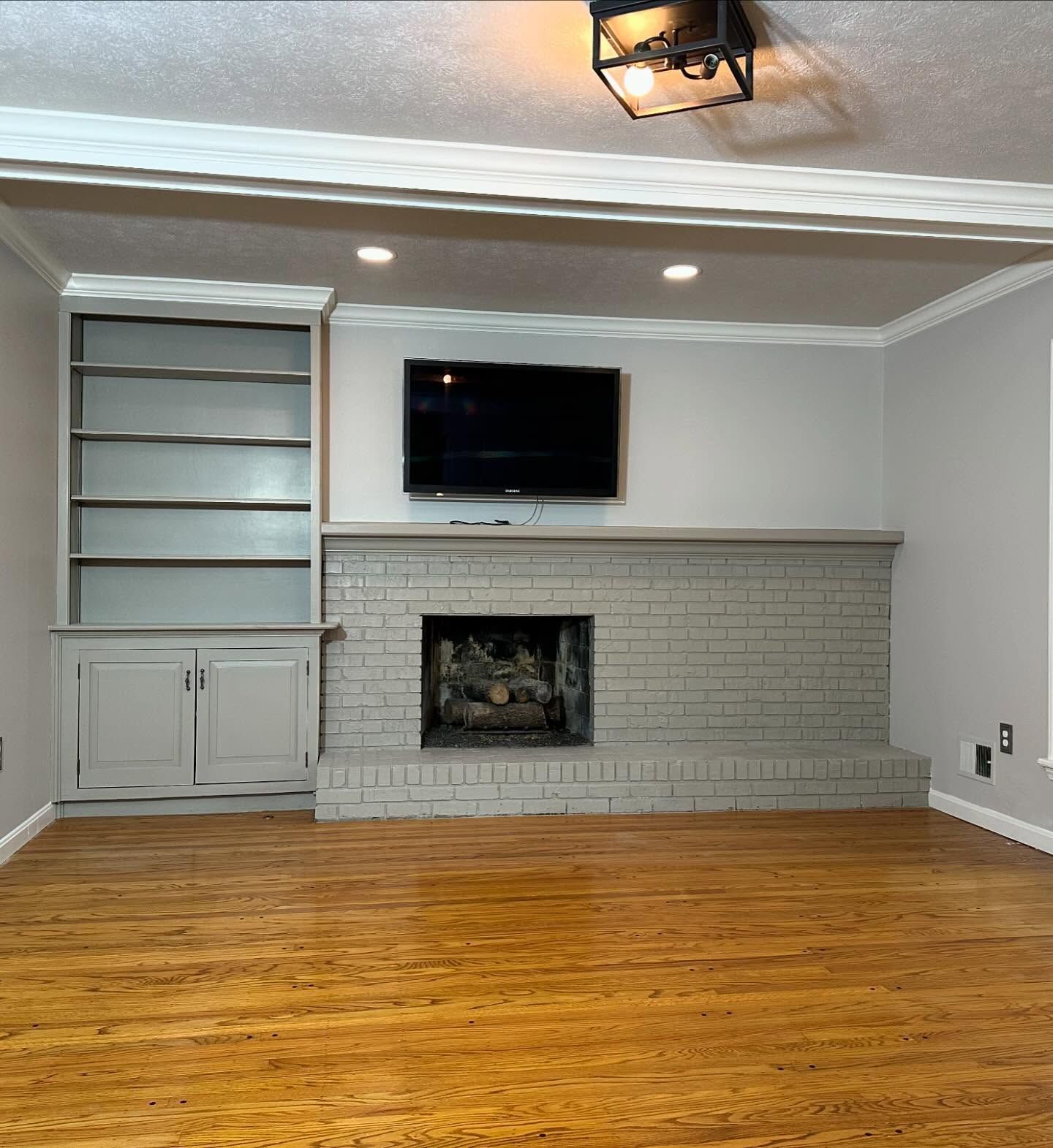 Living room with gray brick fireplace, built-in shelves, wall-mounted TV, and hardwood floor.