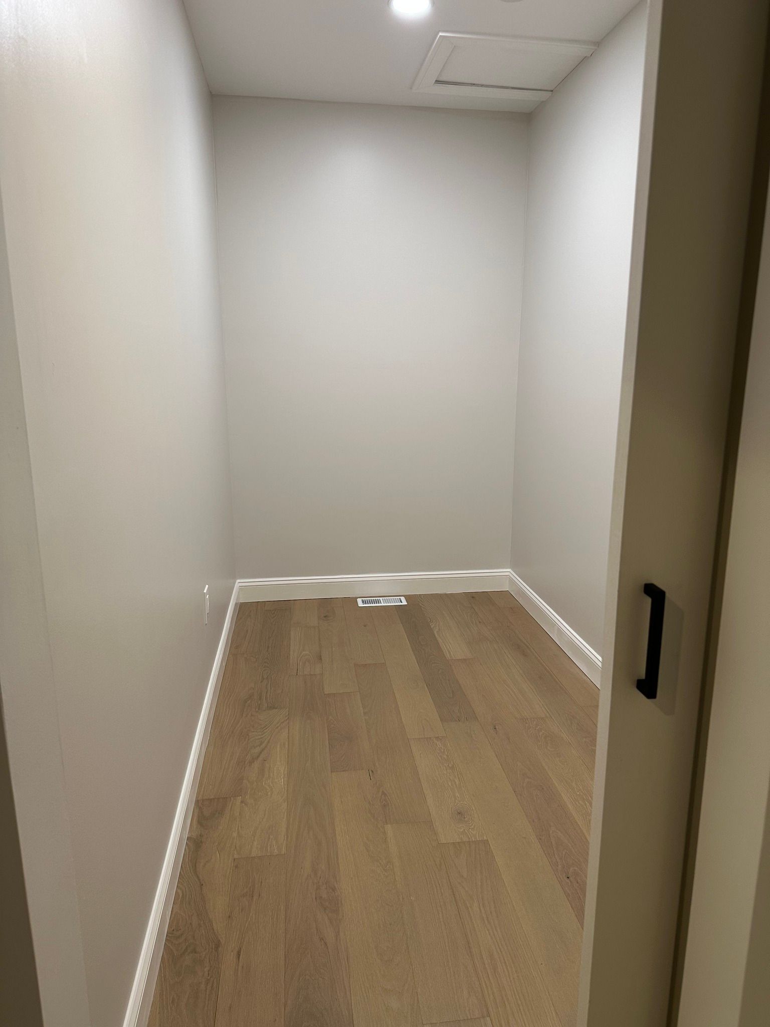 Empty narrow hallway with white walls, wood floor, and a partially open door.