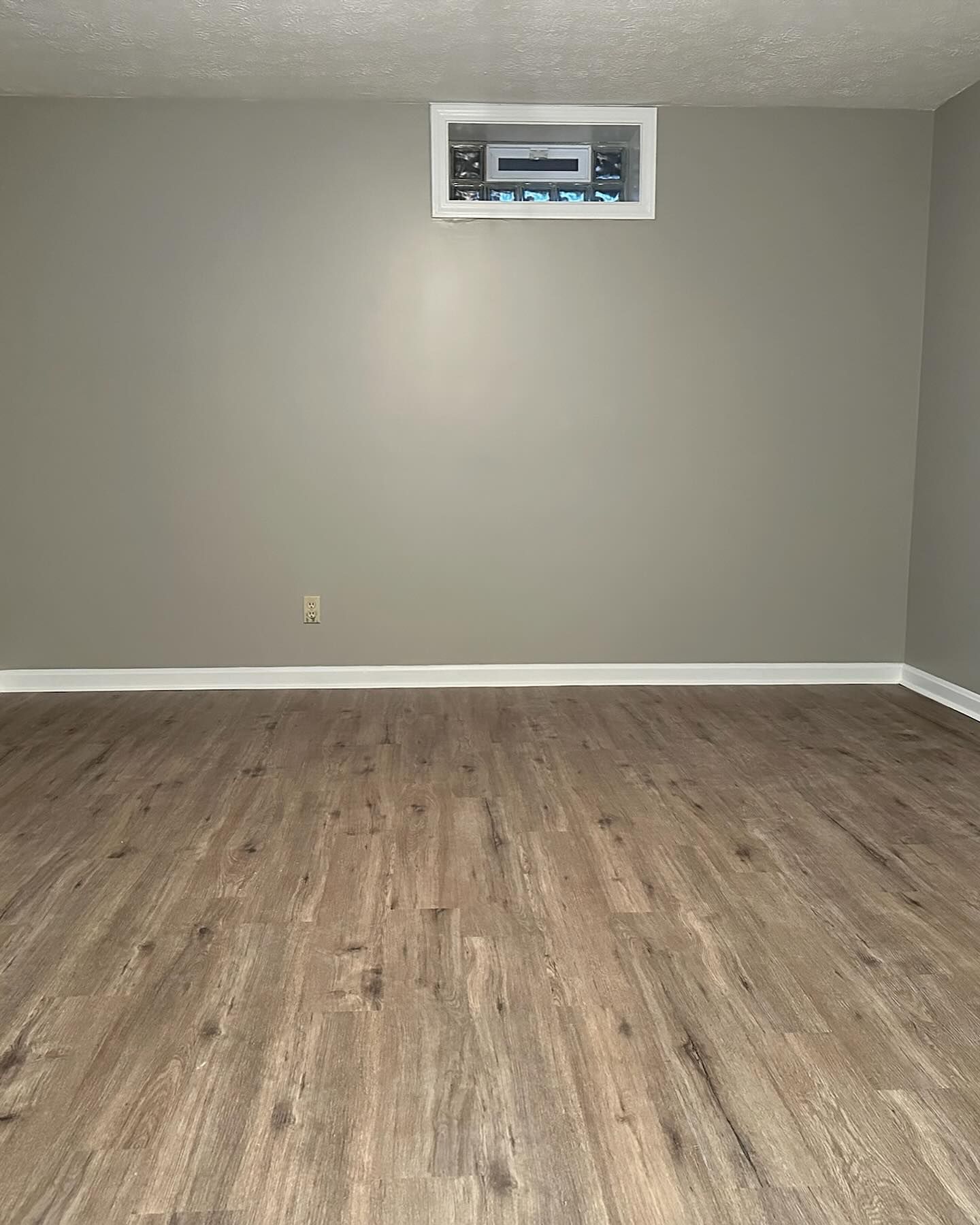 Empty room with gray walls, wood flooring, and a small wall vent near the ceiling.