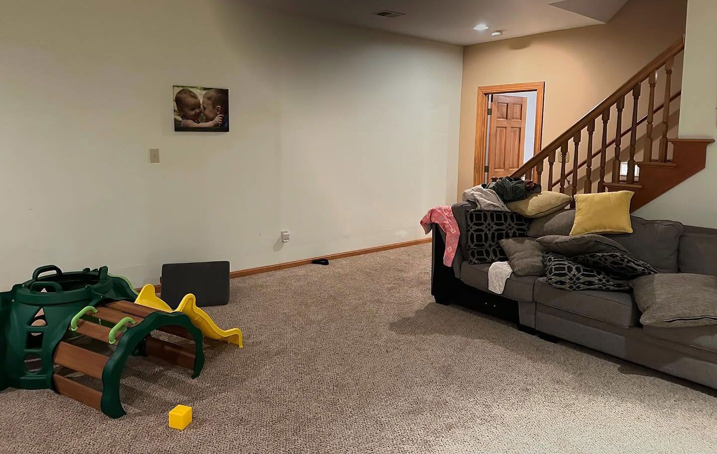 Living room with beige carpet, gray sofa, staircase, and a green plastic toy on the floor.