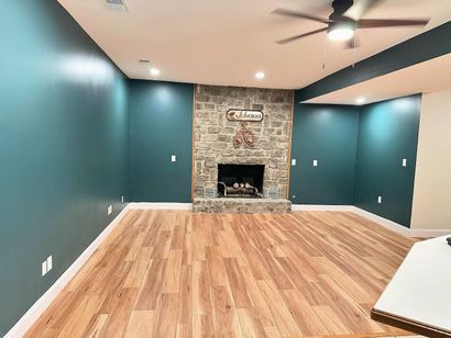 Empty living room with teal walls, wood floors, and a stone fireplace at the far end. Empty living room with teal walls, wood floors, and a stone fireplace at the far end.