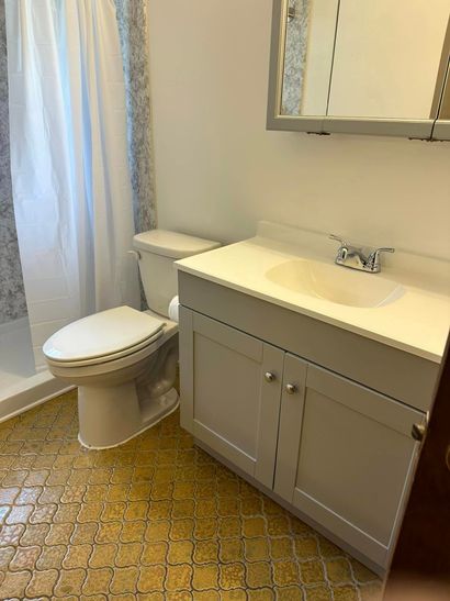 Bathroom with gray vanity, white sink, toilet, mirror, and shower curtain on a patterned floor. Bathroom with gray vanity, white sink, toilet, mirror, and shower curtain on a patterned floor.