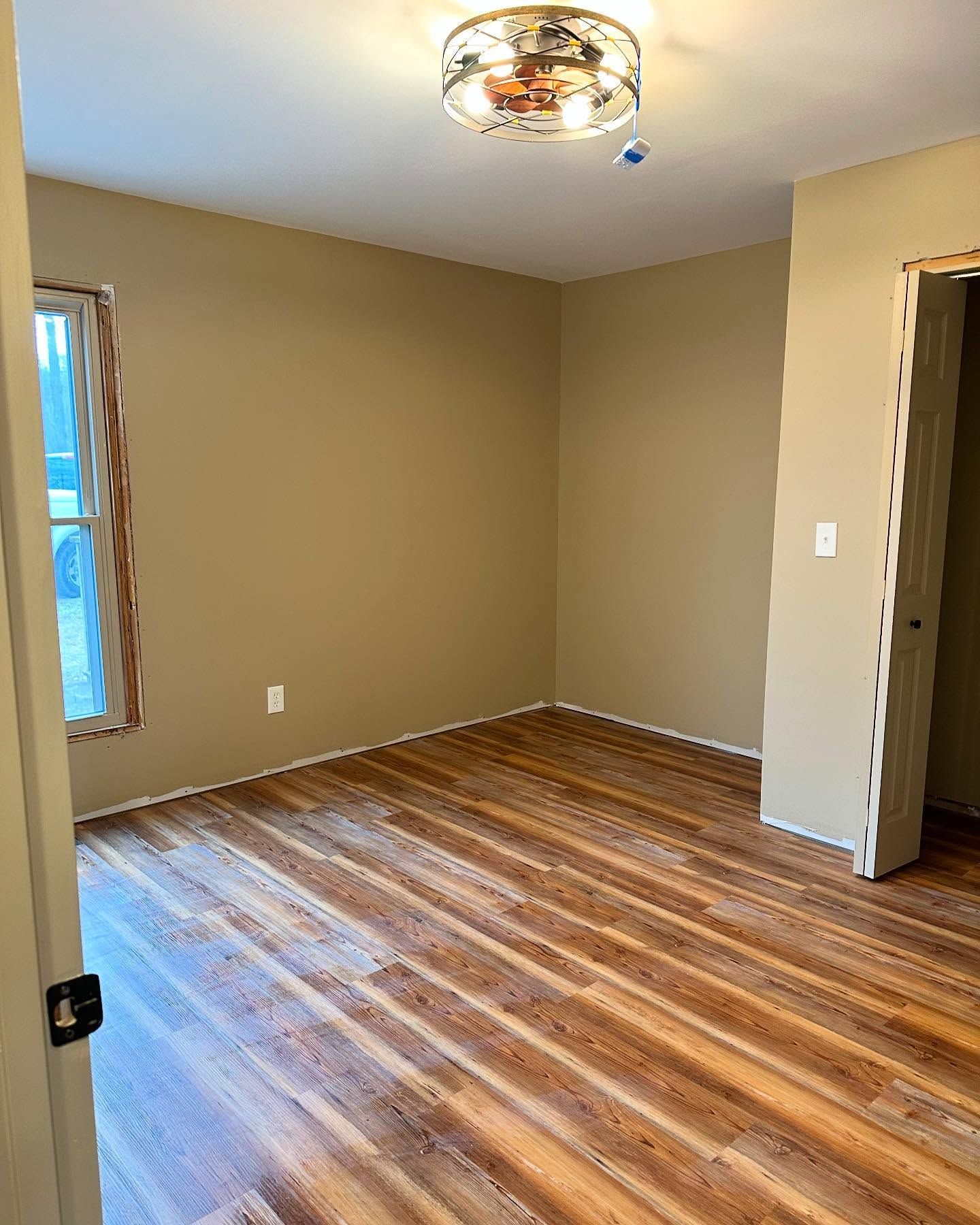 Empty beige room with wood-look floor, ceiling light fixture, and open doorway.