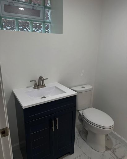 Small bathroom with white vanity, black cabinet, toilet, and window above the sink. Small bathroom with white vanity, black cabinet, toilet, and window above the sink.