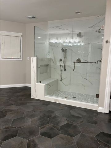Modern bathroom with glass-enclosed shower, white marble tile, and dark hexagon floor tiles Modern bathroom with glass-enclosed shower, white marble tile, and dark hexagon floor tiles