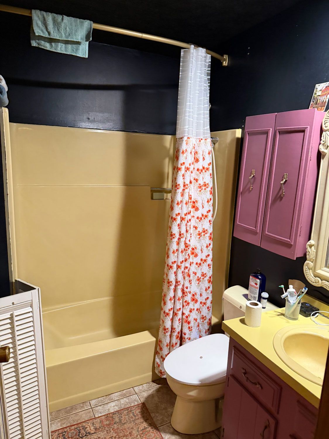 Small bathroom with tan tub, floral shower curtain, pink cabinets, white toilet, and yellow sink vanity. Small bathroom with tan tub, floral shower curtain, pink cabinets, white toilet, and yellow sink vanity.