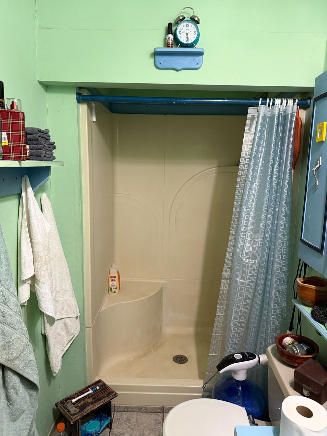 Small bathroom with a shower stall, blue trim, towels, and toiletries on shelves. Small bathroom with a shower stall, blue trim, towels, and toiletries on shelves.