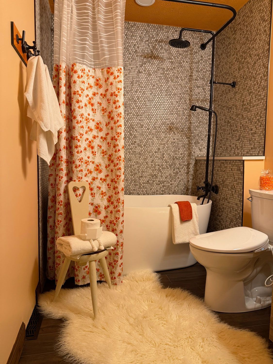 Cozy bathroom with orange walls, floral shower curtain, white toilet, vanity, and fluffy cream rug Cozy bathroom with orange walls, floral shower curtain, white toilet, vanity, and fluffy cream rug