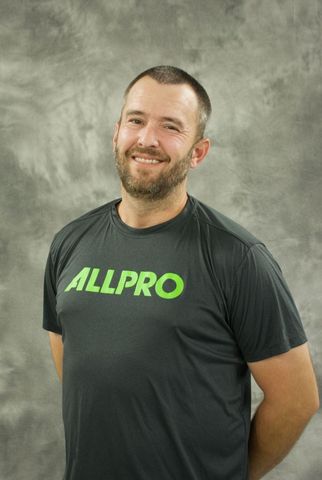 Smiling man in a black ALLPRO T-shirt standing against a gray backdrop Smiling man in a black ALLPRO T-shirt standing against a gray backdrop