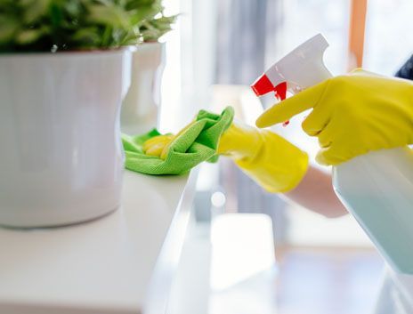 A person is cleaning a table with a spray bottle and a cloth.