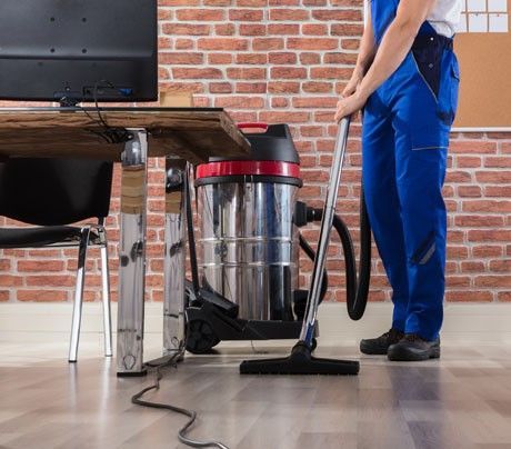 A man is cleaning the floor with a vacuum cleaner in an office.