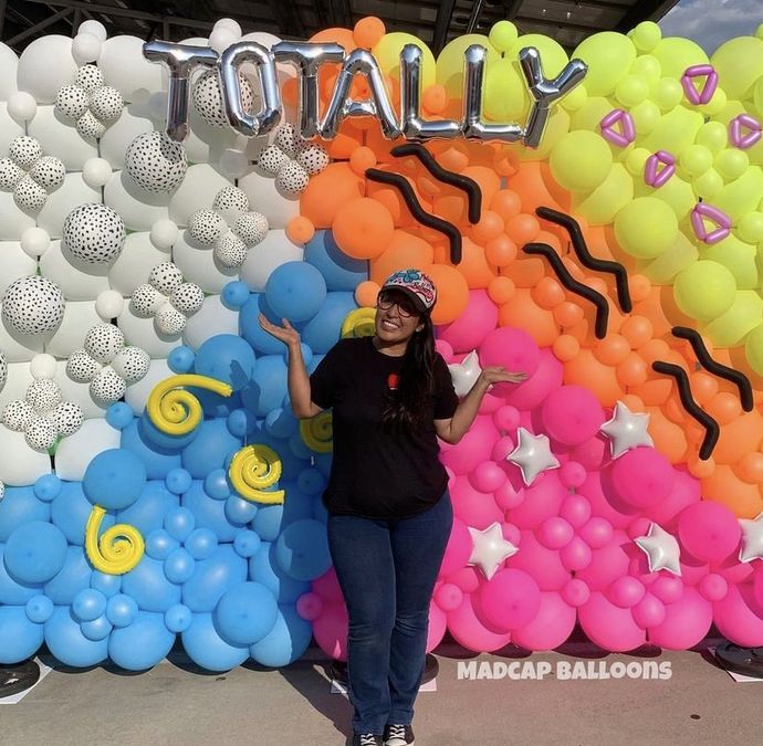 Woman Standing in front of a balloon Wall that says TOTALLY
