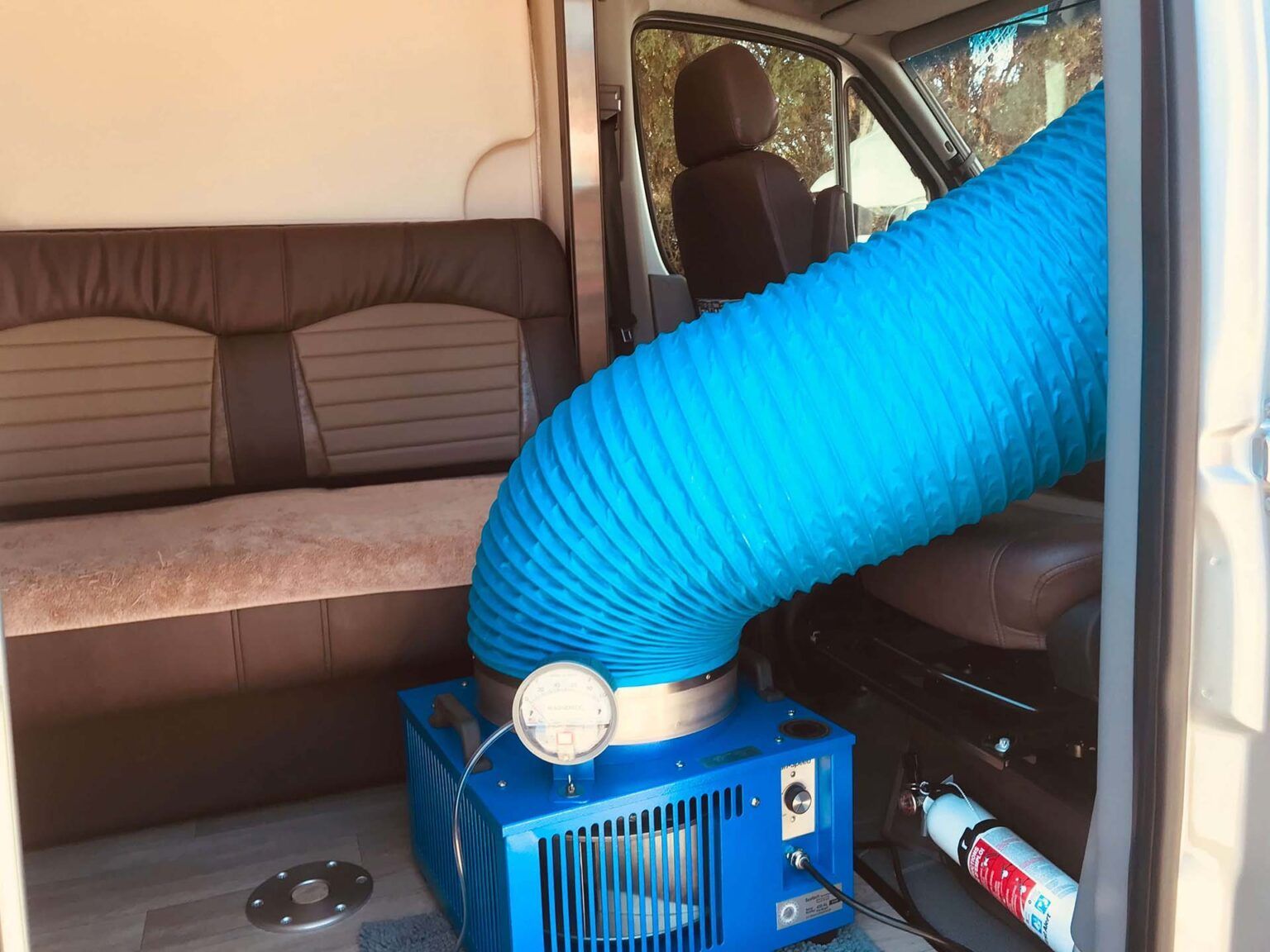Blue heater with hose inside a van. Interior shows seating, driver's seat, and a fire extinguisher.