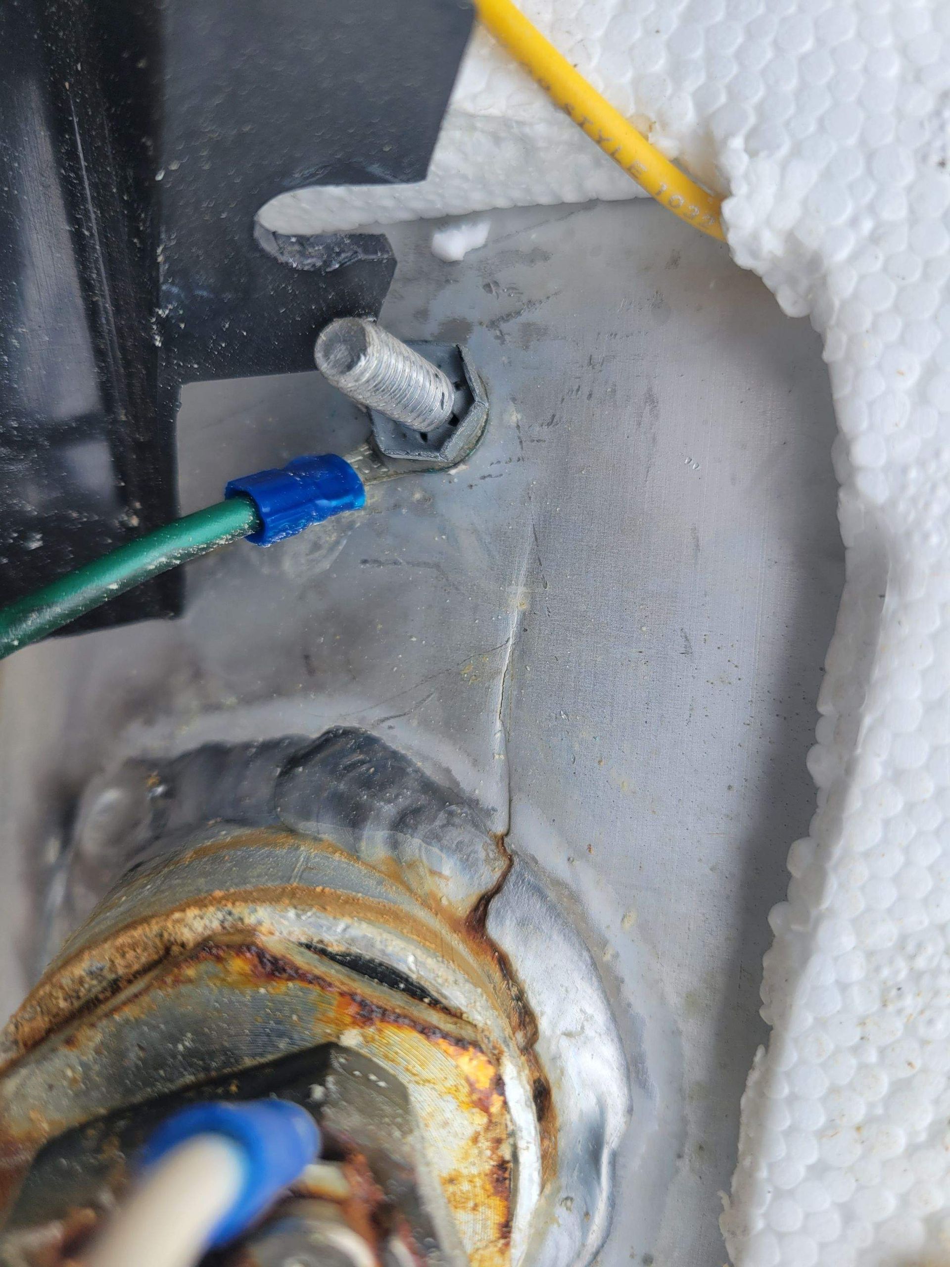 Close-up of a metal fitting with wires connected. Green wire, blue wire connector, and rust visible.