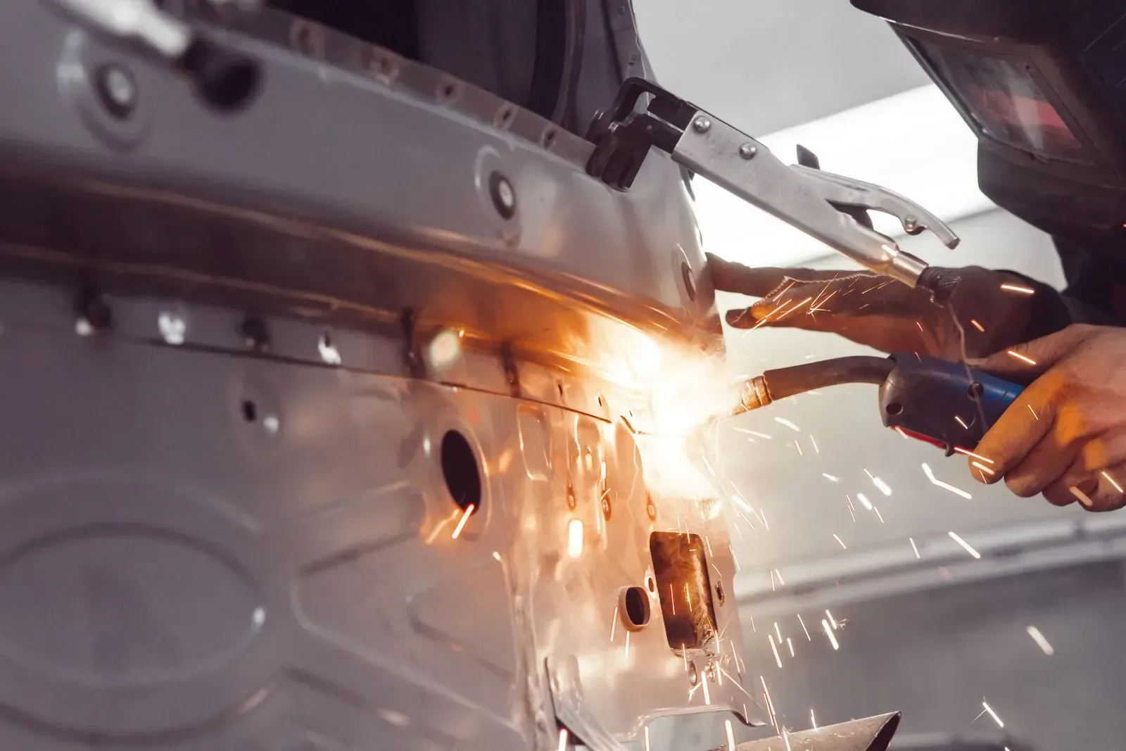 A man is welding a car door in a garage.