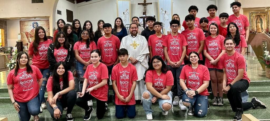 A group of young people in red shirts poses with a clergyman in a church.